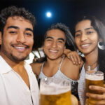 Three people, their faces hidden in shadows clinking glasses filled with beer under the light of a moon.