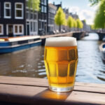 Enjoy a glass of craft beer placed on a rustic wooden table overlooking a picturesque canal in Amsterdam with charming boats and traditional Dutch architecture as the backdrop, on a beautiful sunny day.