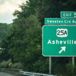 Highway sign for Asheville, North Carolina, exit 51, surrounded by lush green trees.